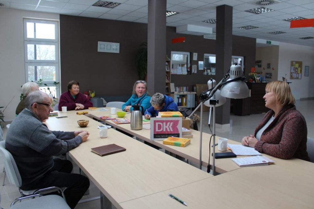 Członkowie Dyskusyjnego Klubu Książki siedzą przy stole i rozmawiają