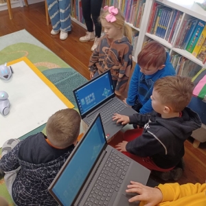 Chłopiec trzyma laptop, czwórka dzieci patrzy na robota