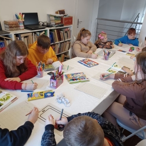 Grupa dzieci siedzi przy stole, rysują