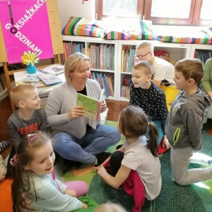 Opiekun czyta zgromadzonym wokół dzieciom książkę