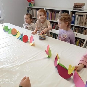 Dzieci siedzą przy stole razem z wykonanymi przez siebie pracami plastycznymi