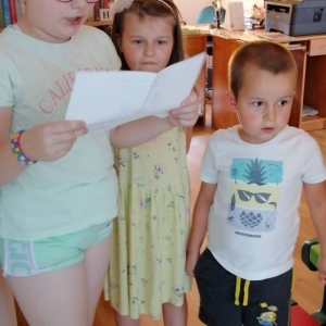 Dzieci stoją obok dziewczynki trzymającej kartkę