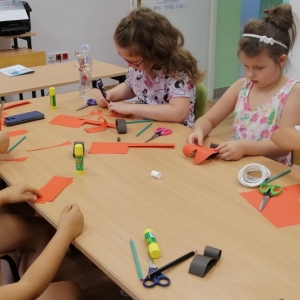 Dzieci siedzące przy stole wycinają kolorowy papier 