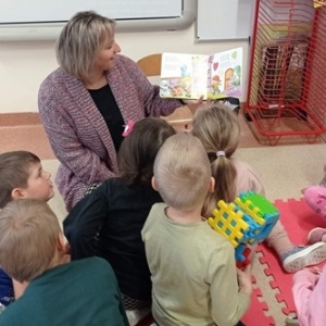 Dzieci przyglądają się obrazkom w książce pokazywanej przez opiekuna