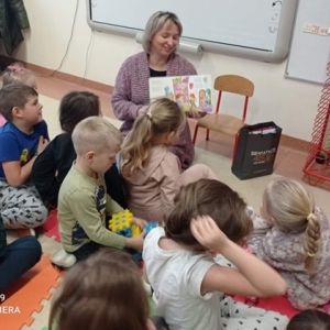 Opiekun pokazuje dzieciom siedzącym na matach obrazki w książce