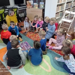 Grupa dzieci siedzi na dywanie i słucha opowiadania bibliotekarki