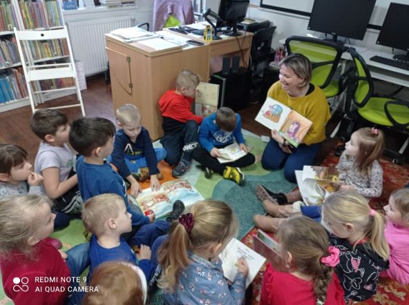 Bibliotekarka prezentuje książkę dzieciom siedzącym na podłodze